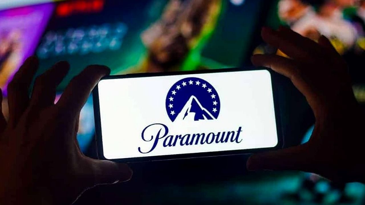 Logotipo da Paramount exibido na tela de celular segurado por mãos diante de conteúdo em streaming ao fundo