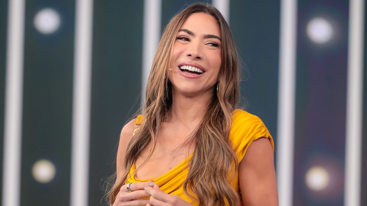 Patricia Abravanel sorri durante apresentação de programa do SBT usando vestido amarelo.