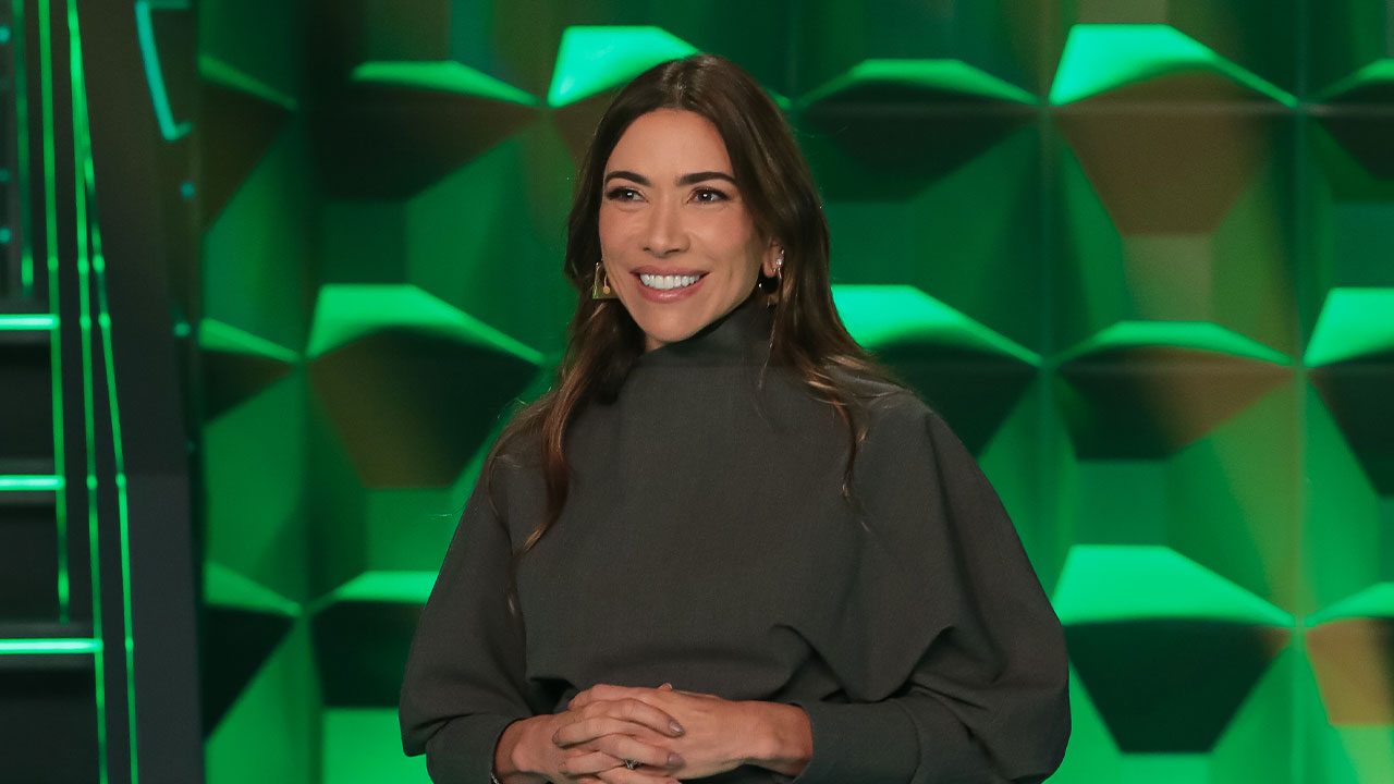 Patricia Abravanel sorrindo no palco do Show do Milhão com cenário iluminado em verde ao fundo