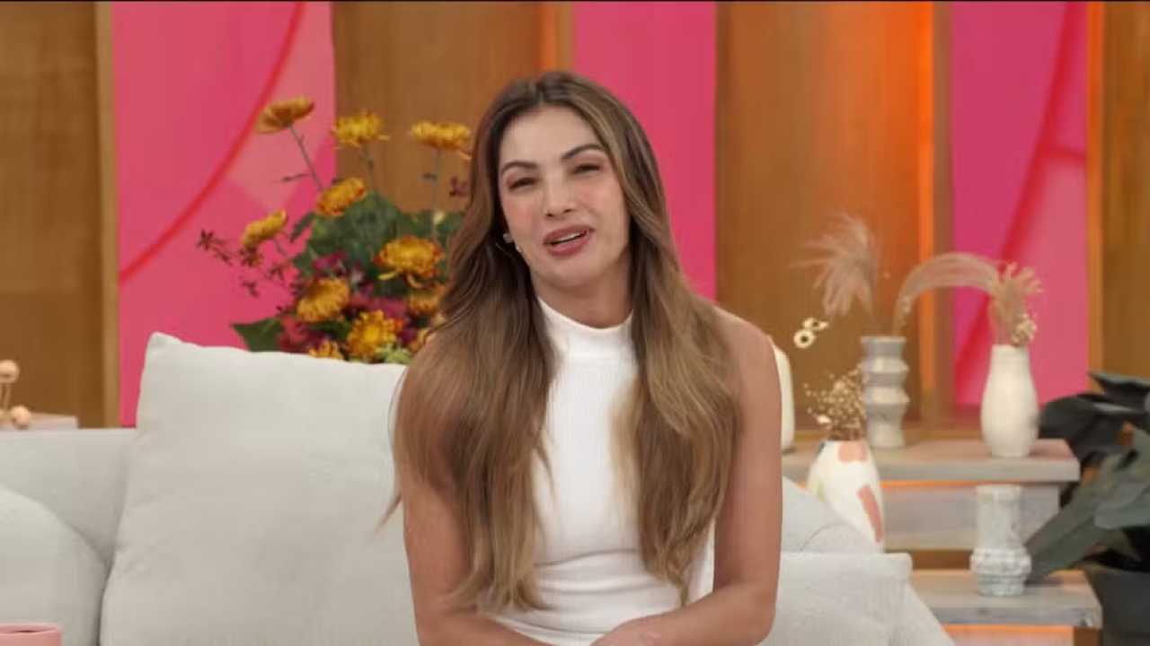 Patrícia Poeta em um fundo rosa e sentada em um sofá claro