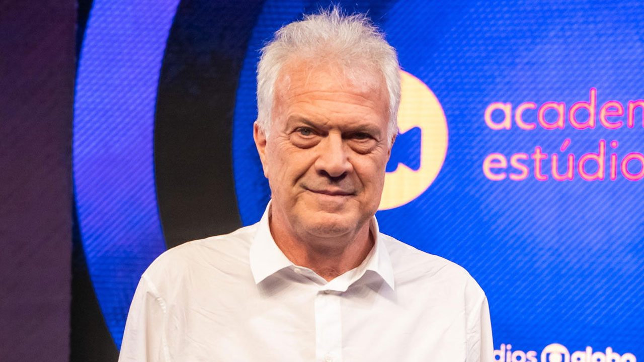 Pedro Bial com camisa branca diante de painel azul com logotipo e texto Academia dos Estúdios Globo