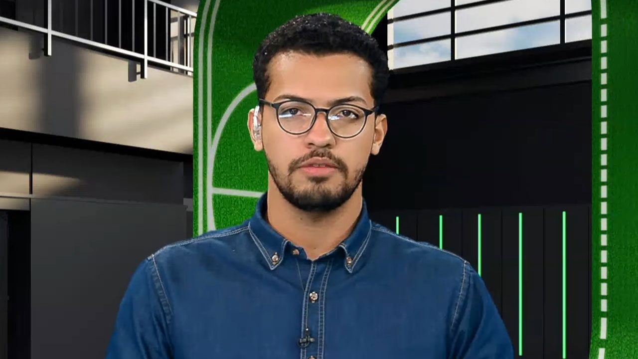 Pedro Oliveira de óculos e camisa jeans azul olha sério para a câmera no estúdio da Xsports com fundo verde e linhas brancas atrás