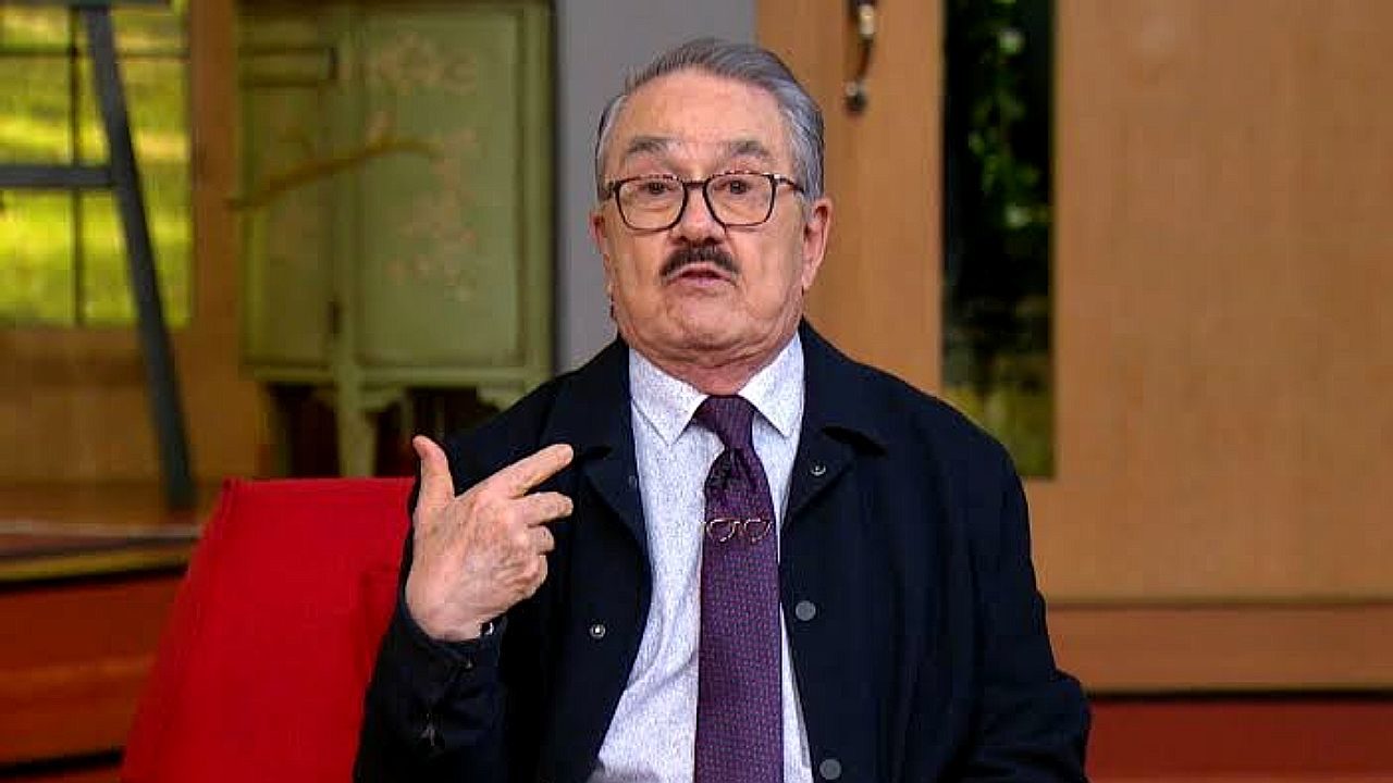 Pedro Sola gesticula durante participação em programa de TV com terno, gravata e óculos no estúdio