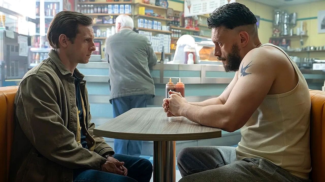 Dois homens conversam sentados em lanchonete durante cena de série ou filme