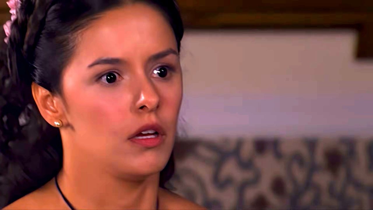Isaura, interpretada por Bianca Rinaldi, com expressão surpresa e olhos arregalados reage durante cena da novela A Escrava Isaura, gravada em ambiente interno com sofá ao fundo.