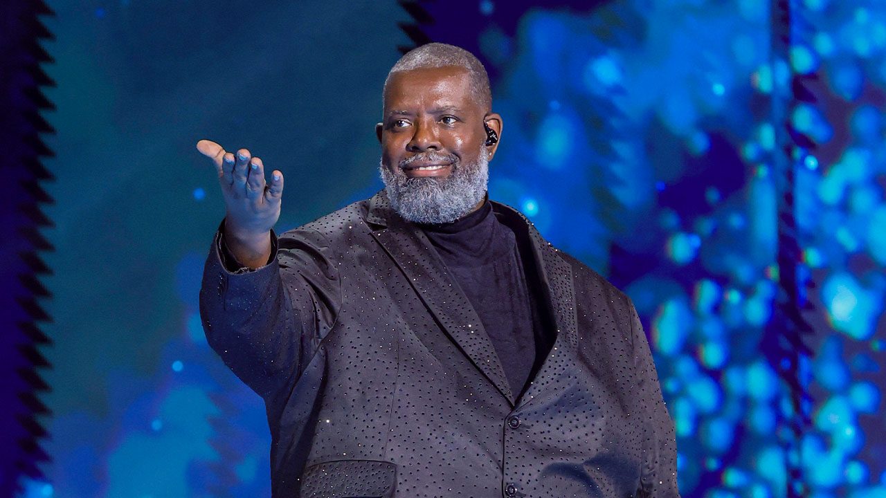 Péricles com figurino preto estendendo a mão durante apresentação no show de 60 anos da TV Globo