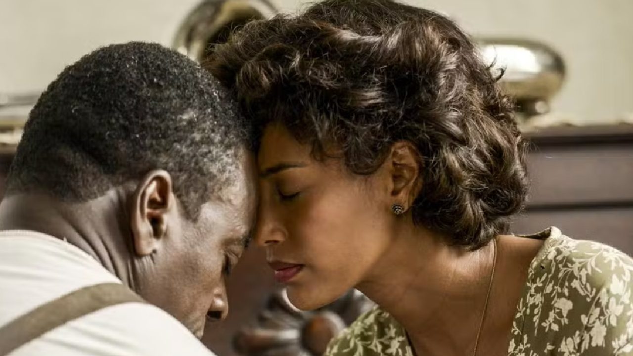 Casal em momento íntimo encosta as testas com olhos fechados, transmitindo consolo e conexão emocional em ambiente doméstico de época