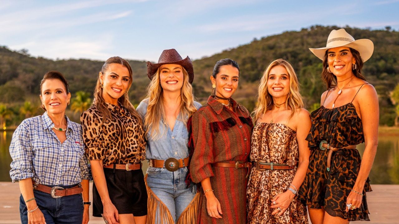 Seis mulheres posam sorrindo ao ar livre em frente a paisagem de cerrado usando roupas com estilo country em cena de divulgação do programa Poderosas do Cerrado