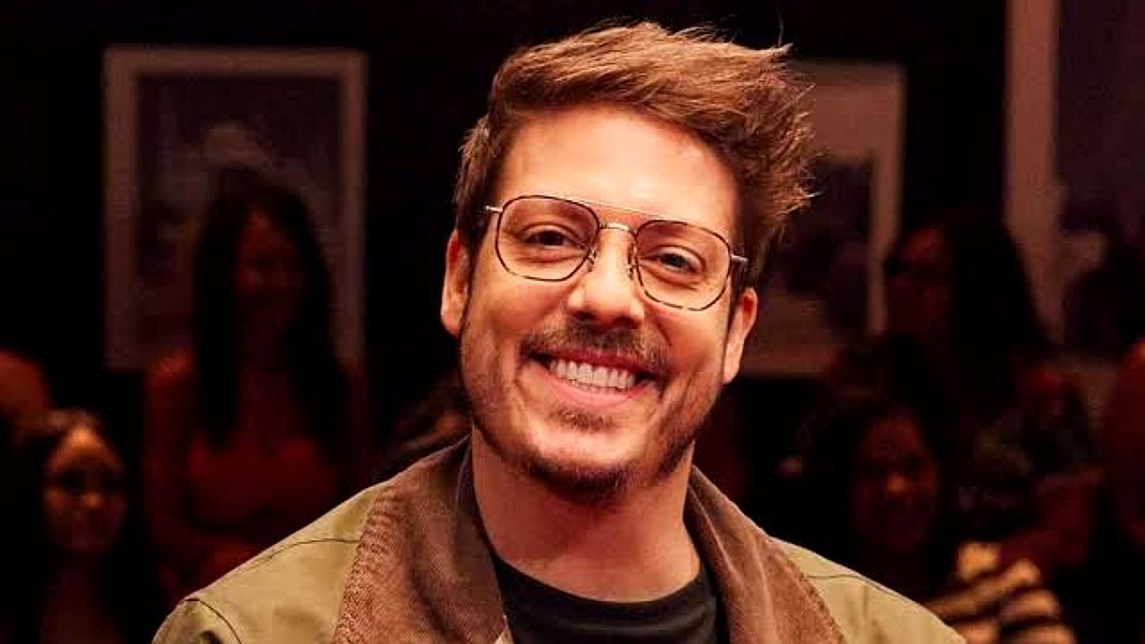 Fábio Porchat sorri usando óculos durante gravação de programa de entrevistas com plateia ao fundo
