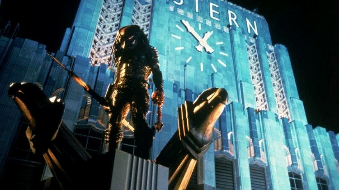 Predador alienígena armado em frente a um prédio