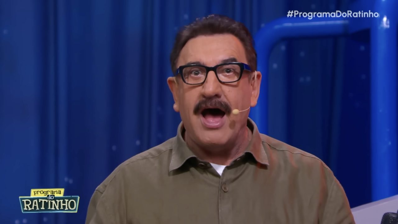 Ratinho, de camisa verde e óculos, fala com expressão surpresa no palco do Programa do Ratinho