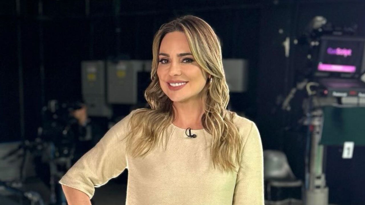 Rachel Sheherazade sorri com blusa bege em estúdio com câmeras ao fundo durante bastidores de gravação de programa