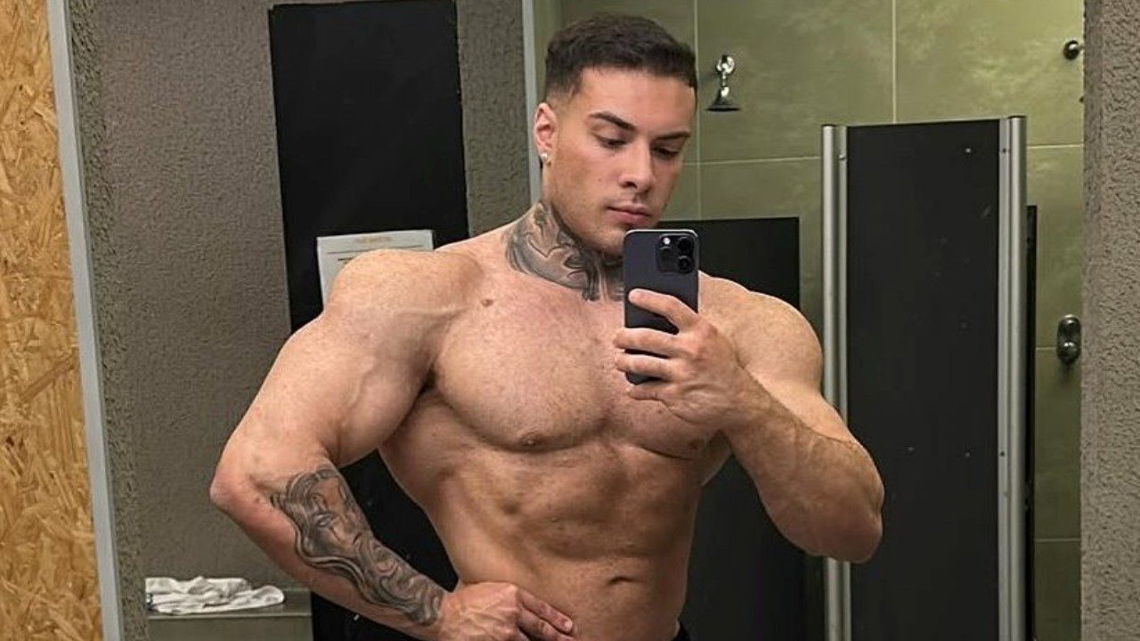 Rafa Marttinz posa sem camisa para selfie no espelho de um banheiro, exibindo o corpo musculoso, tatuagens no pescoço e braço, e segurando celular