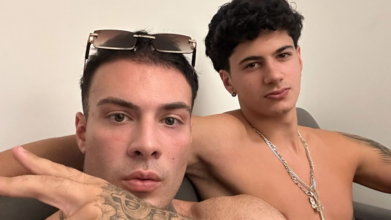 Rafa Marttinz com óculos na cabeça e mão tatuada em destaque ao lado de Davi Martins que usa correntes de prata em ambiente de iluminação clara