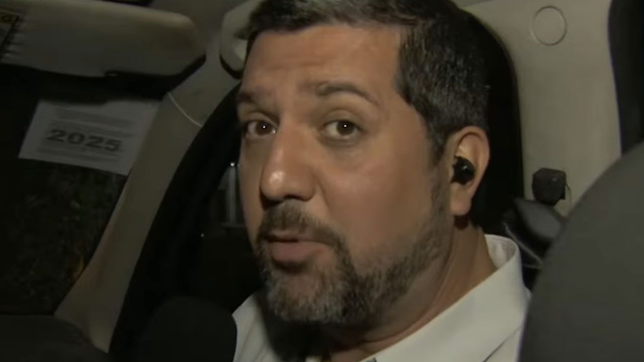 Rafael Batalha com fone de ouvido dentro de carro durante entrada ao vivo no Brasil Urgente da Band