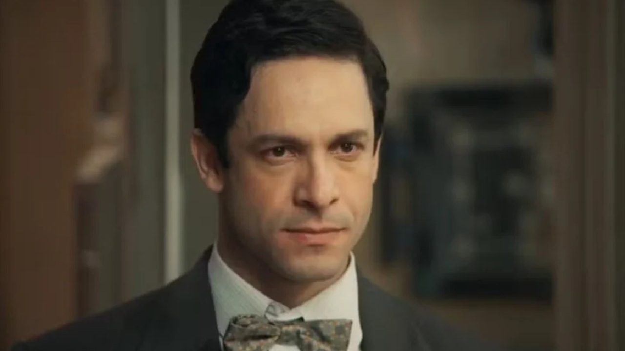 Homem de terno e gravata borboleta com expressão séria em ambiente interno