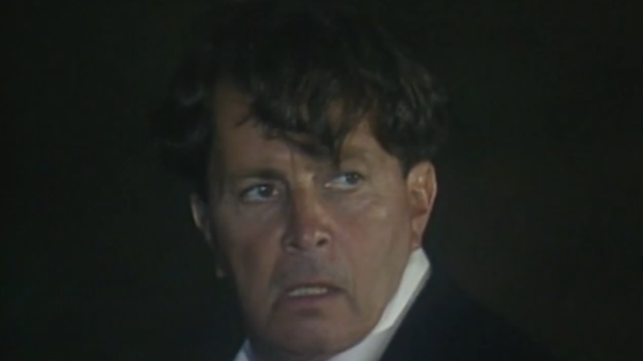 Cena da novela Rainha da Sucata mostra um homem com expressão tensa e olhar assustado, em ambiente escuro e de clima misterioso