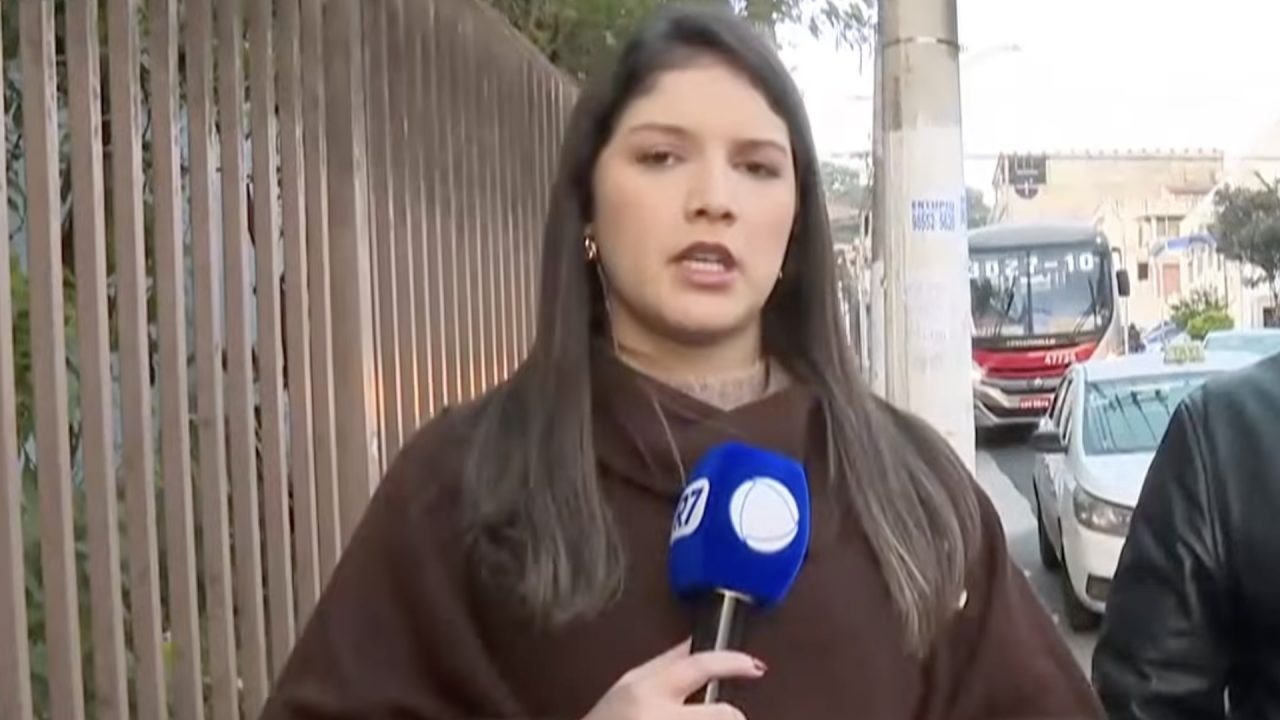 Ranny Oliveira segura microfone da Record durante entrada ao vivo em calçada com ônibus e carros ao fundo no Balanço Geral Manhã