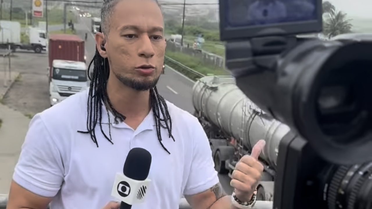 Raphael Mascarenhas, repórter de afiliada da Globo, com uma camisa branca e uma rodovia atrás