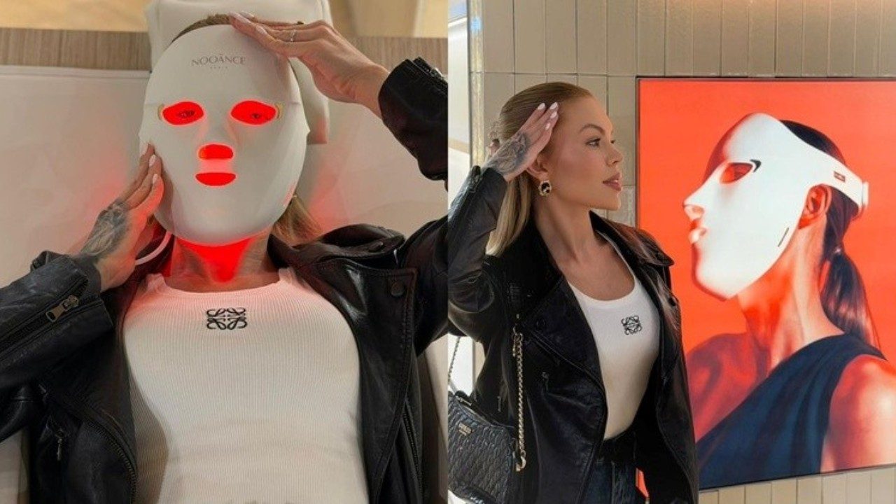 Ravena Hanniely usa máscara facial de LED vermelho e posa ao lado de painel com imagem do equipamento estético