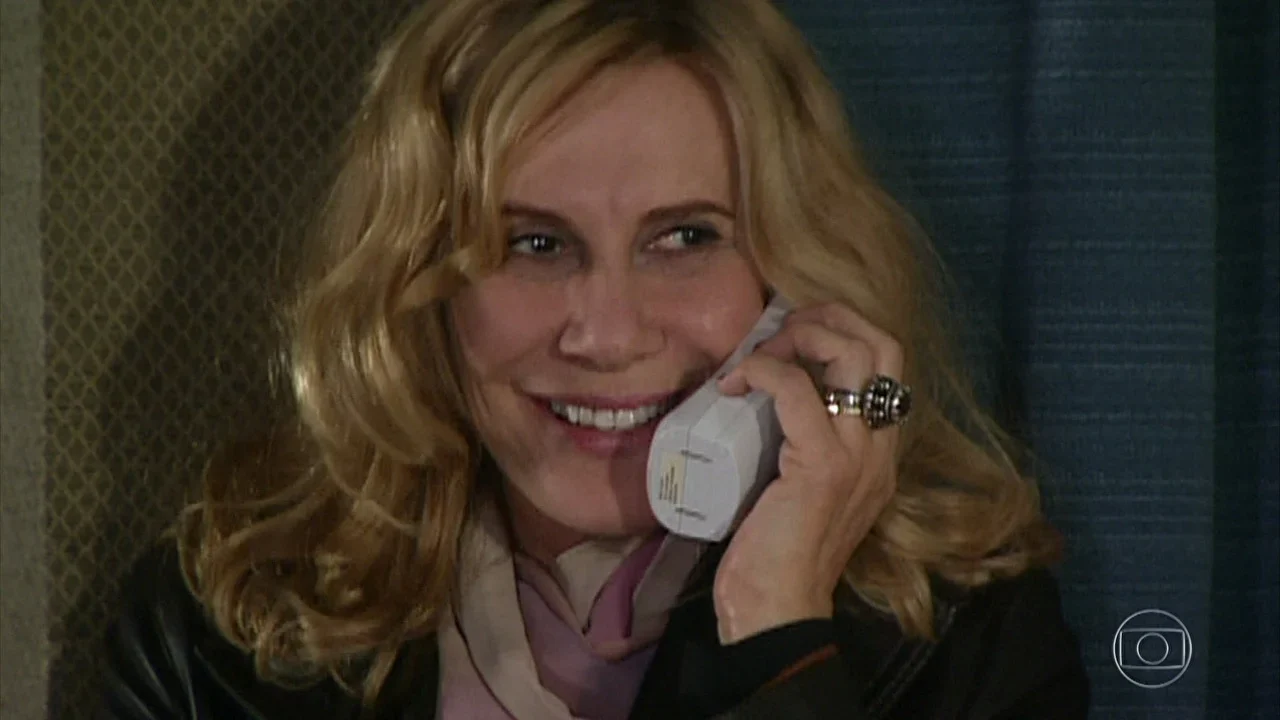 Renata Sorrah sorrindo enquanto fala ao telefone em cena de novela da TV Globo