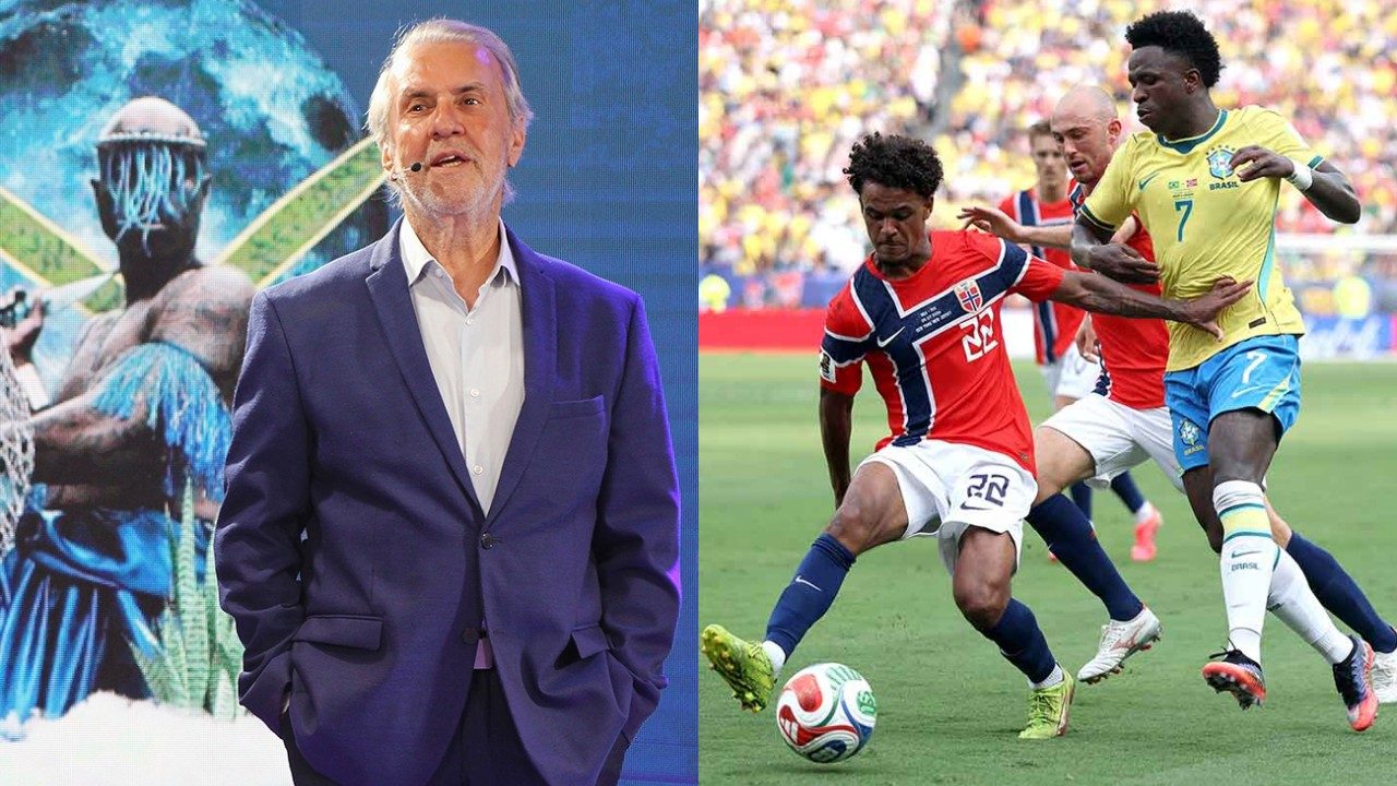 Robério de Ogum de blazer azul em palco com telão ao fundo ao lado de lance da seleção brasileira contra a Noruega