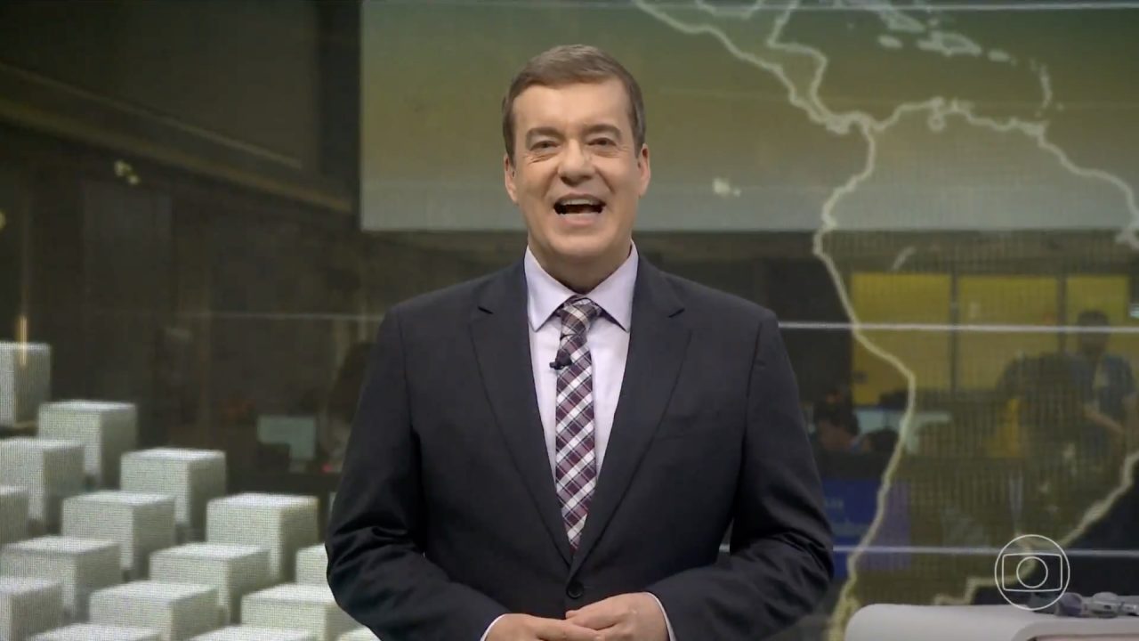 Roberto Kovalick, de terno escuro, sorri no estúdio do Jornal Hoje, com mapa ao fundo