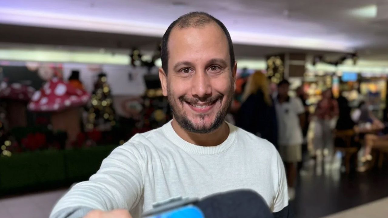 Rodrigo Assis sorrindo em ambiente decorado com temas natalinos e fundo desfocado de shopping center