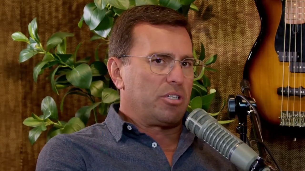 Rodrigo Bocardi, com camisa escura e óculos, fala em um microfone profissional durante participação em um podcast