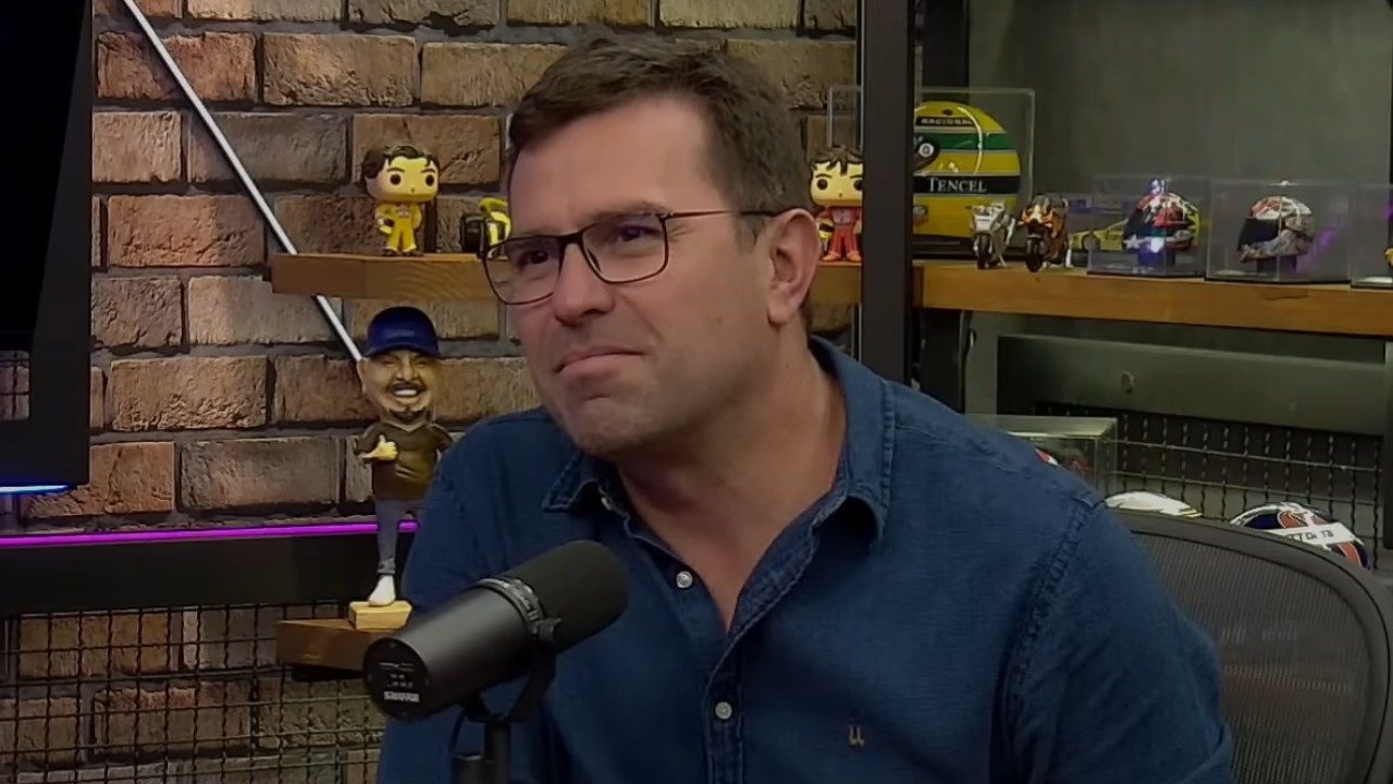 Rodrigo Bocardi fala ao microfone em estúdio de podcast com prateleiras e objetos decorativos ao fundo