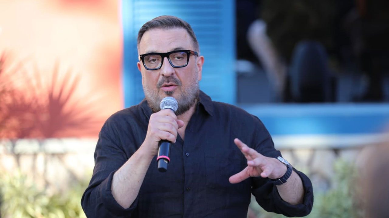 Rodrigo Carelli fala ao microfone usando camisa preta e óculos de grau durante coletiva de imprensa de A Fazenda