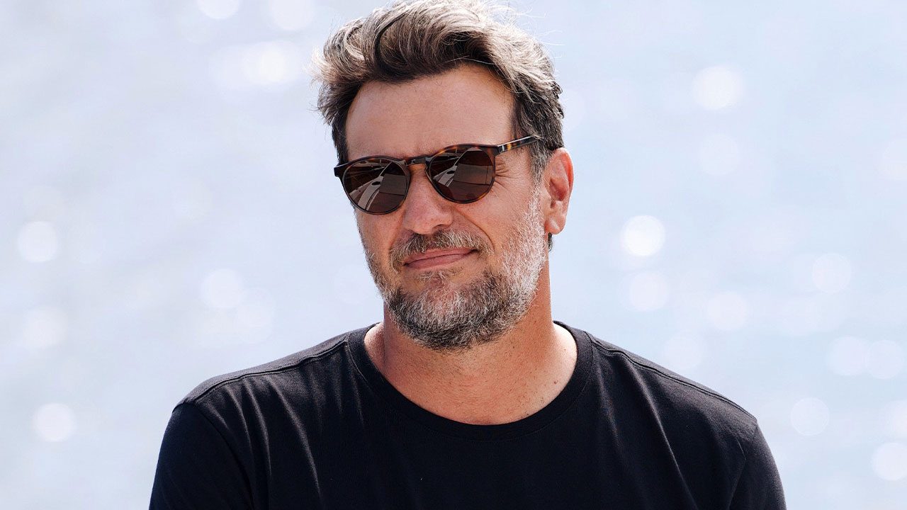 Rodrigo Lombardi com óculos escuros e camiseta preta caracterizado como Molina em Mania de Você