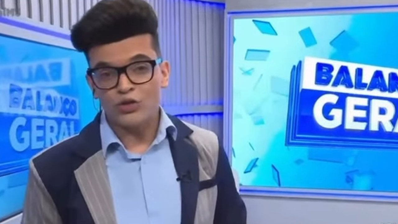 Rodrigo Nascimento, com topete e óculos, usa blazer e camisa azul no estúdio do Balanço Geral MS, telejornal da afiliada da Record