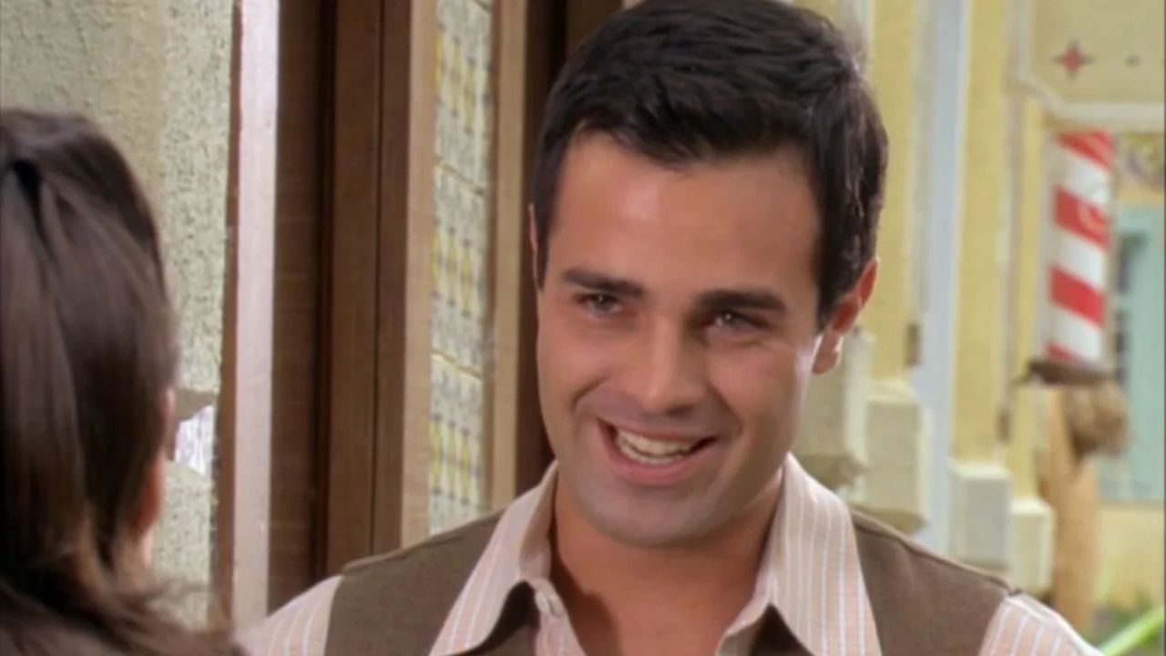 Rodrigo Phavanello sorri durante conversa em cena ambientada em rua de novela
