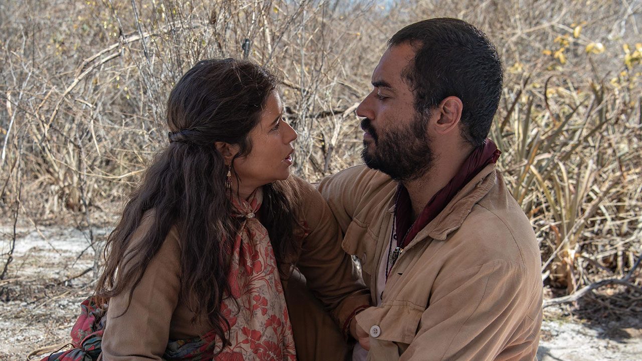 Rosa (Isadora Cruz) e Josué (Thomas Aquino) sentados e se olhando em cena de Guerreiros do Sol, do Globoplay Novelas
