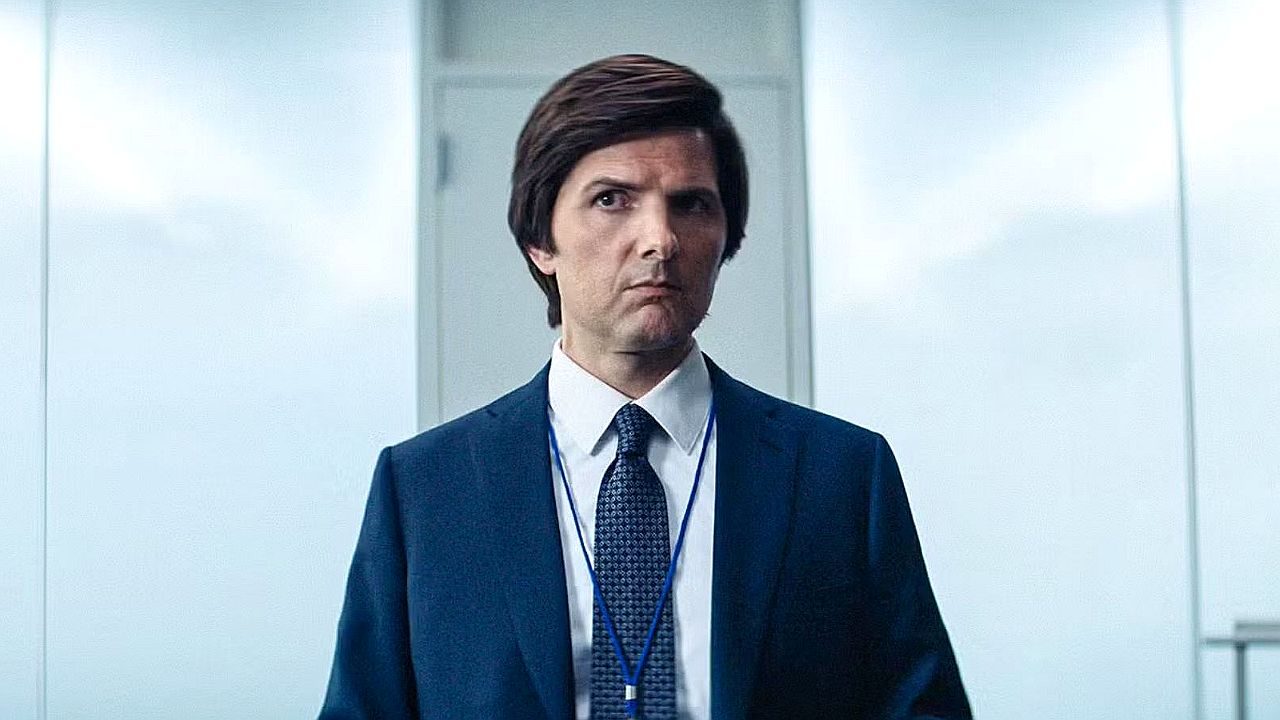 Homem de terno e crachá observa com expressão séria em ambiente corporativo com paredes claras ao fundo