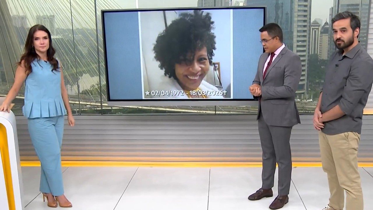 Sabina Simonato, Marcelo Pereira e Guilherme Pimentel observam tela com foto de mulher sorrindo, em estúdio do Bom Dia São Paulo com vista da cidade