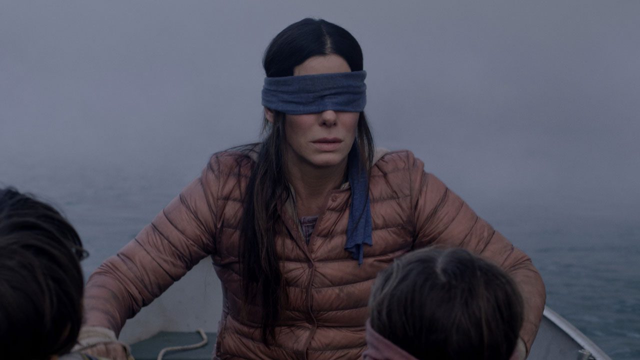 A atriz Sandra Bullock com uma venda nos olhos em cena de suspense no barco em um rio no filme Bird Box