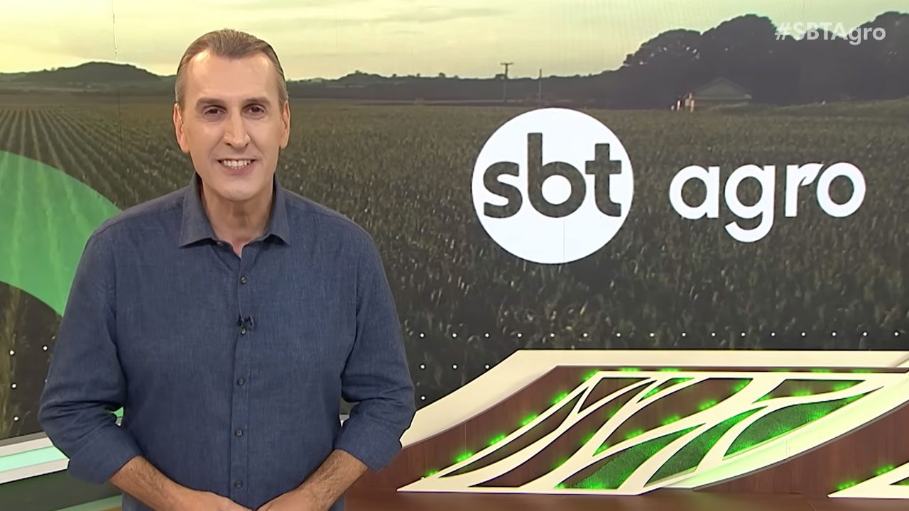 Sandro Ivanowski apresenta o SBT Agro em estúdio com painel de lavoura ao fundo e logotipo do programa