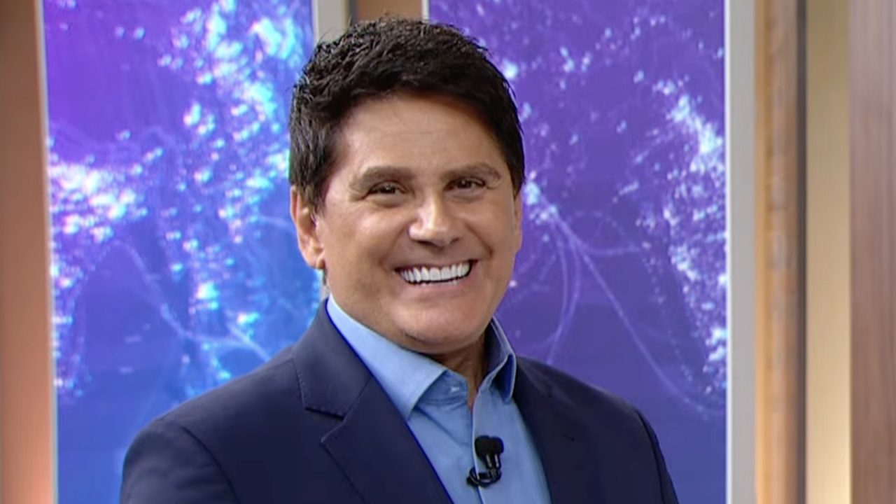 Cesar Filho, de terno azul, sorri no estúdio do SBT Brasil com painel em tons de azul ao fundo