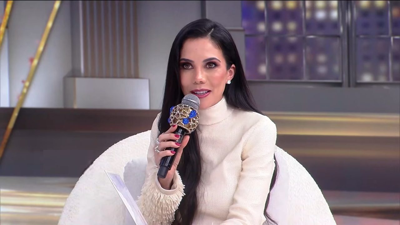 Daniela Albuquerque, usando um vestido claro, segura microfone e fala durante o Sensacional, programa de auditório exibido na RedeTV!.