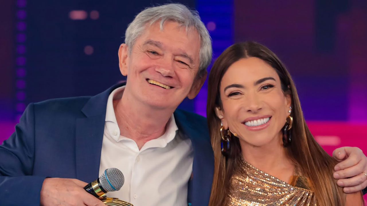 Serginho Groisman com microfone e Patrícia Abravanel sorrindo abraçados no palco do Programa Silvio Santos