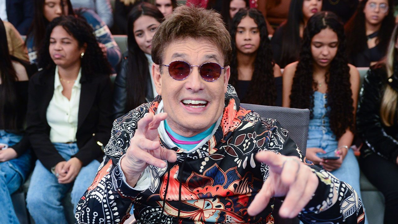 Sérgio Mallandro de óculos escuros e blusa estampada no quadro Dez ou Mil do Programa do Ratinho com plateia ao fundo