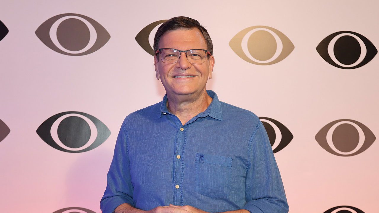 Sérgio Maurício sorri diante de painel com logotipos da Band durante evento da emissora