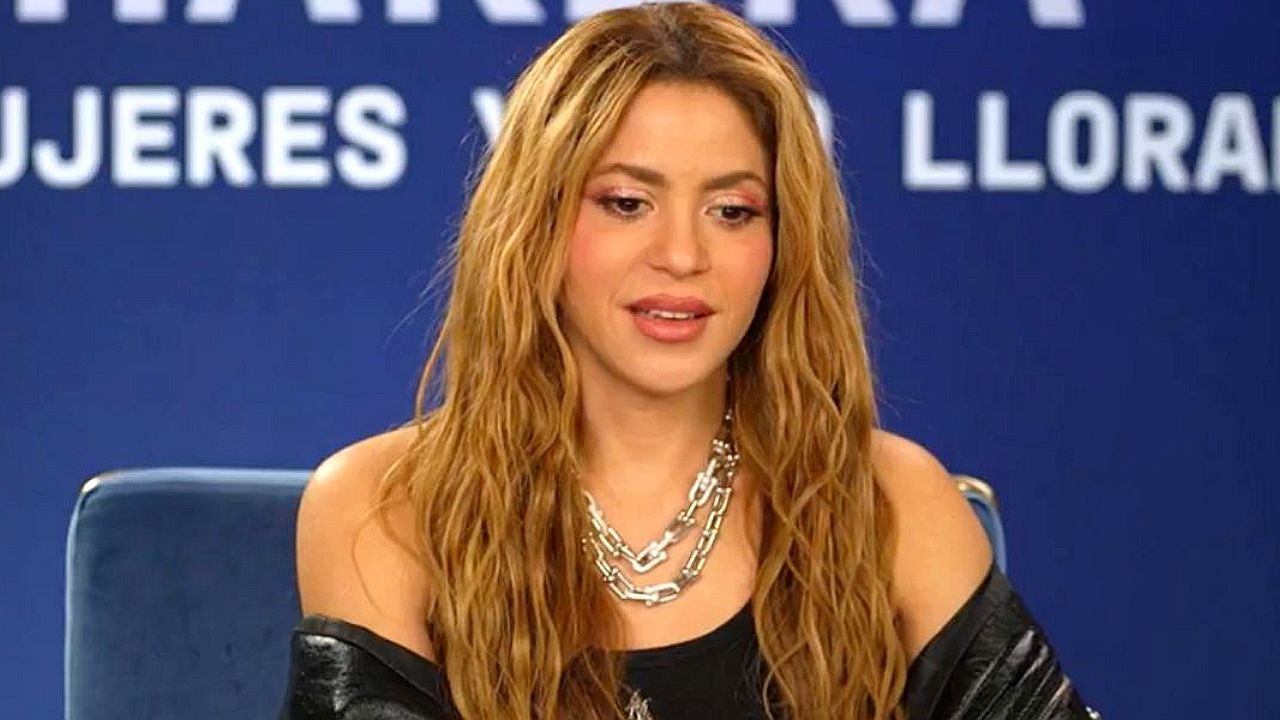 Cantora de cabelos longos participa de coletiva de imprensa diante de painel azul com texto em espanhol