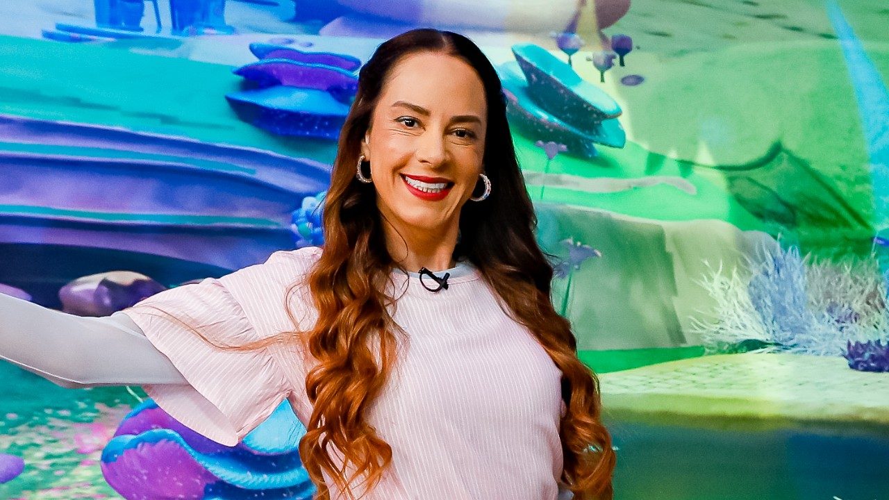 Silvia Abravanel sorri em estúdio do Sábado Animado diante de cenário colorido com elementos de animação ao fundo