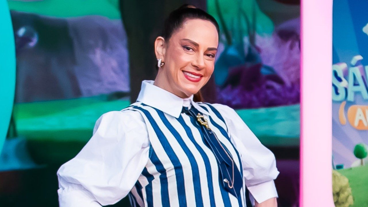 Silvia Abravanel sorri no cenário do Sábado Animado usando vestido listrado azul e branco com mangas bufantes e cabelo preso