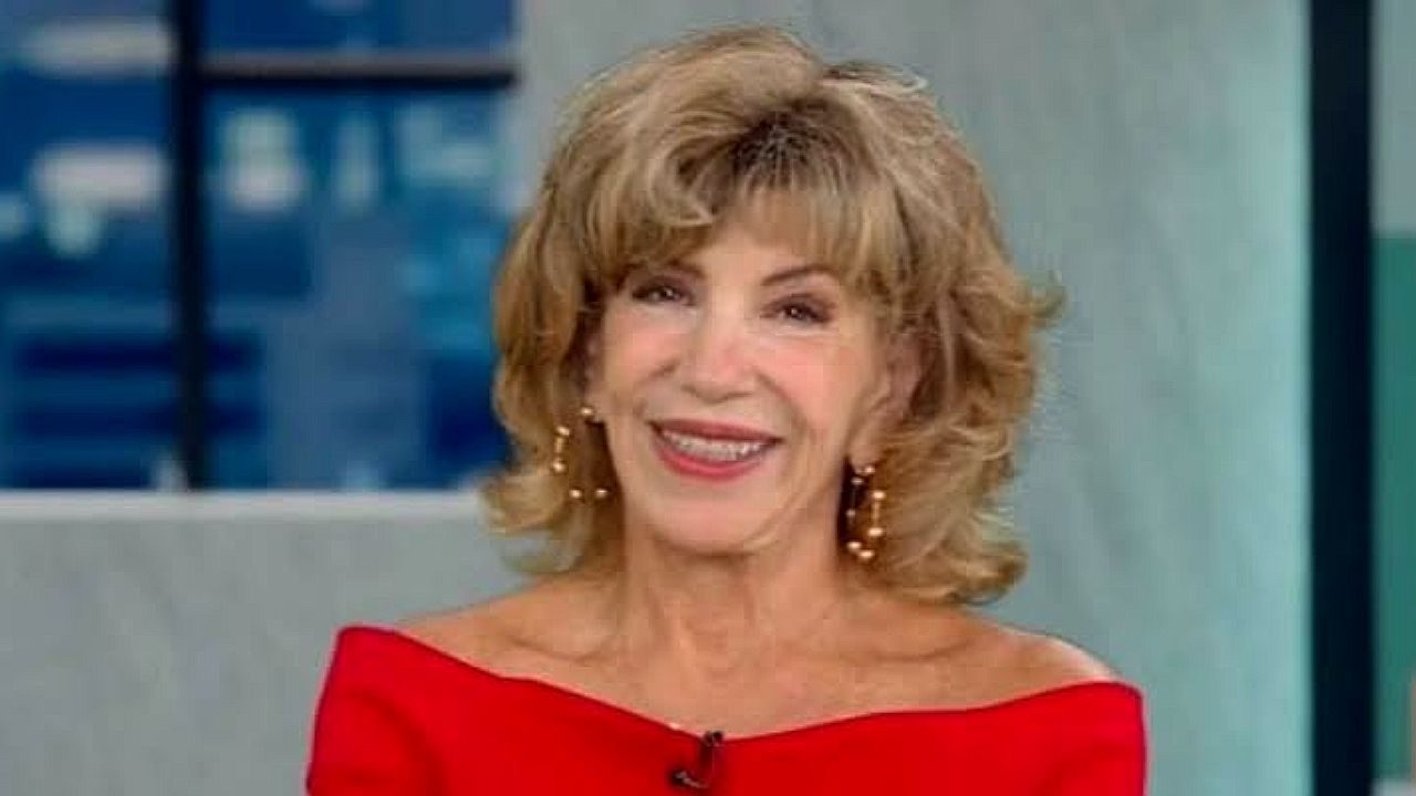 Silvia Poppovic sorri durante participação em programa de televisão usando vestido vermelho de ombros à mostra