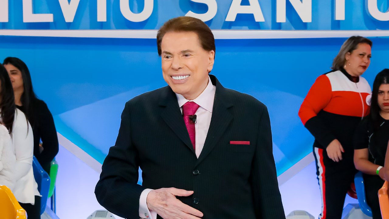Silvio Santos sorrindo no palco do Programa Silvio Santos com plateia ao fundo no SBT