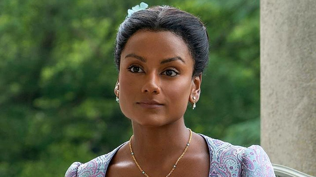 Atriz com cabelo preso e expressão séria em cenário externo em cena de novela de época